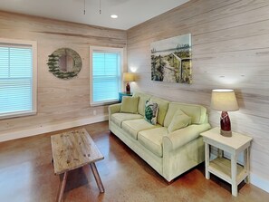 Uma sala de estar com um sofá verde claro, uma mesa de madeira pequena e uma luminária sobre uma mesinha lateral.