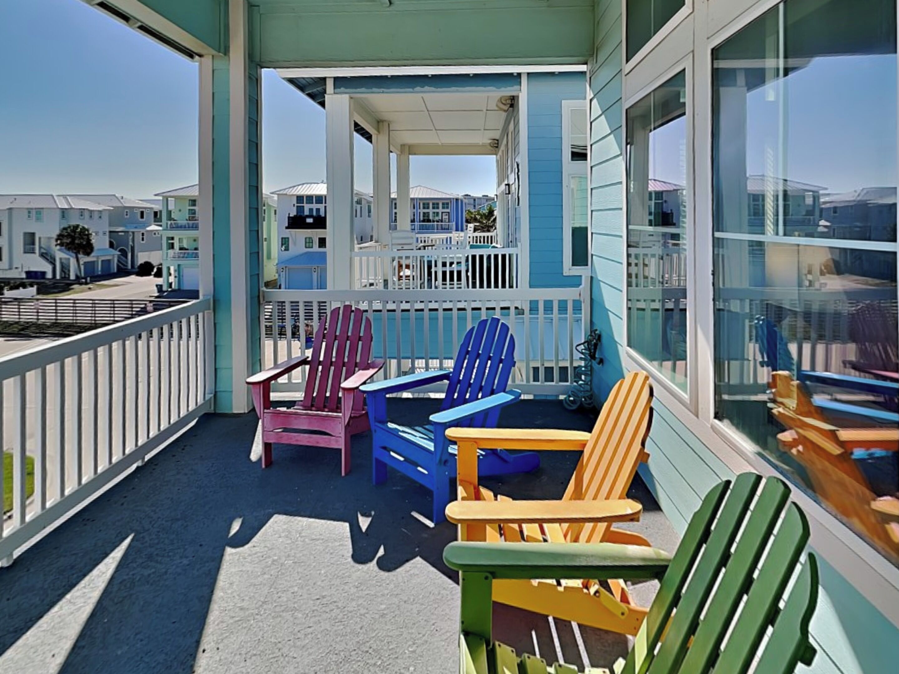 Un balcon agrémenté de chaises Adirondack aux couleurs vives, offrant une vue sur d’autres immeubles.