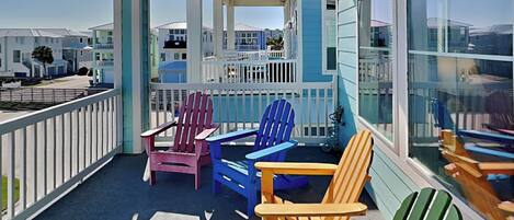 Un balcon agrémenté de chaises Adirondack aux couleurs vives, offrant une vue sur d’autres immeubles.
