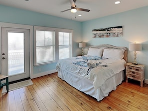 A bedroom with a bed, two bedside tables, a ceiling fan, and a painting on the wall.