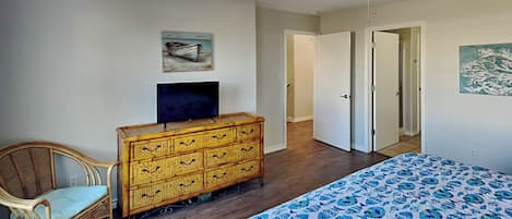 Ein Schlafzimmer mit einem Bett, einem Fernseher auf einer Holzkommode, einem Korbstuhl und einem Deckenventilator.