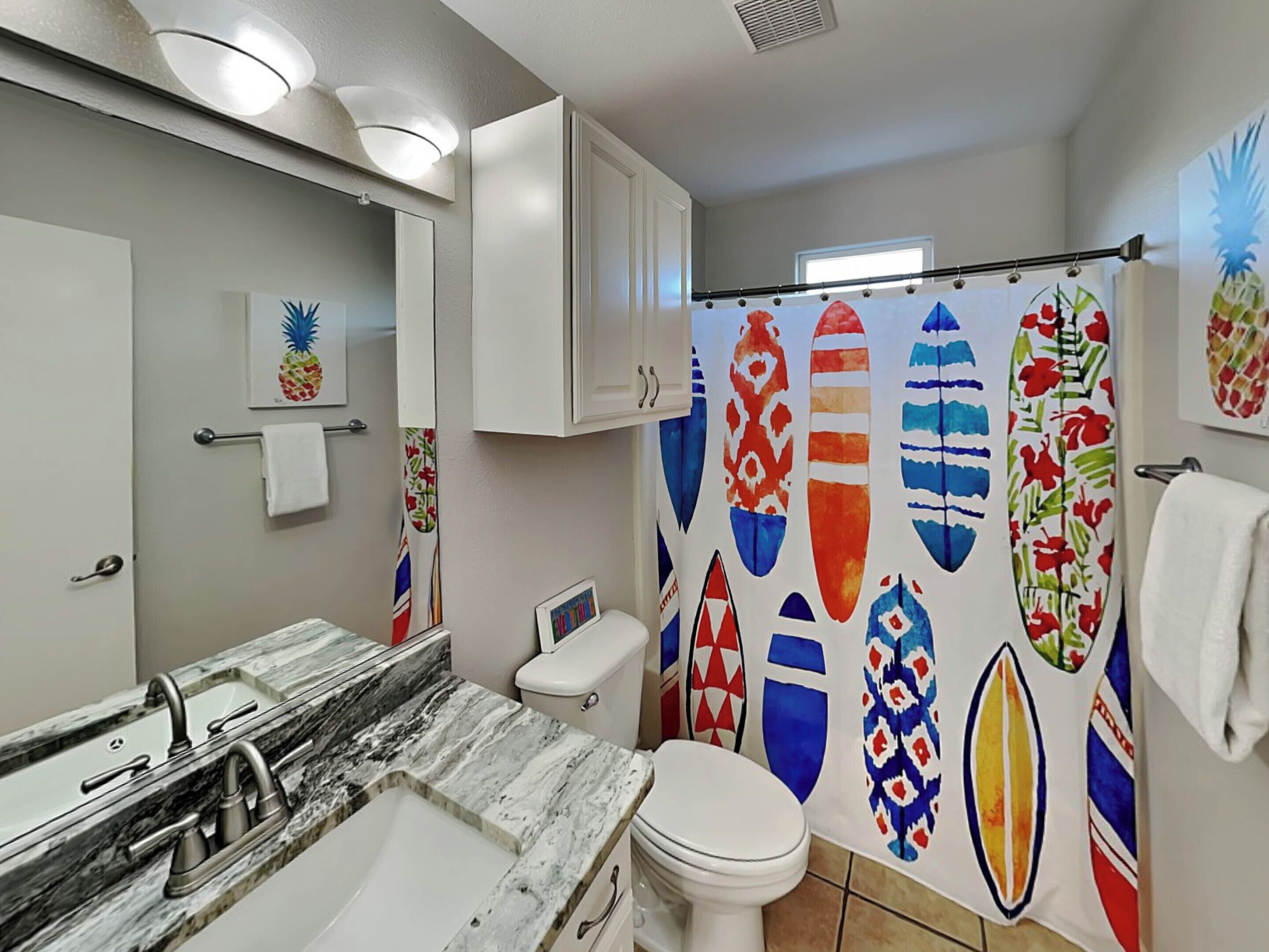 A bathroom with a marble sink, white toilet, and a shower curtain with surfboard designs.