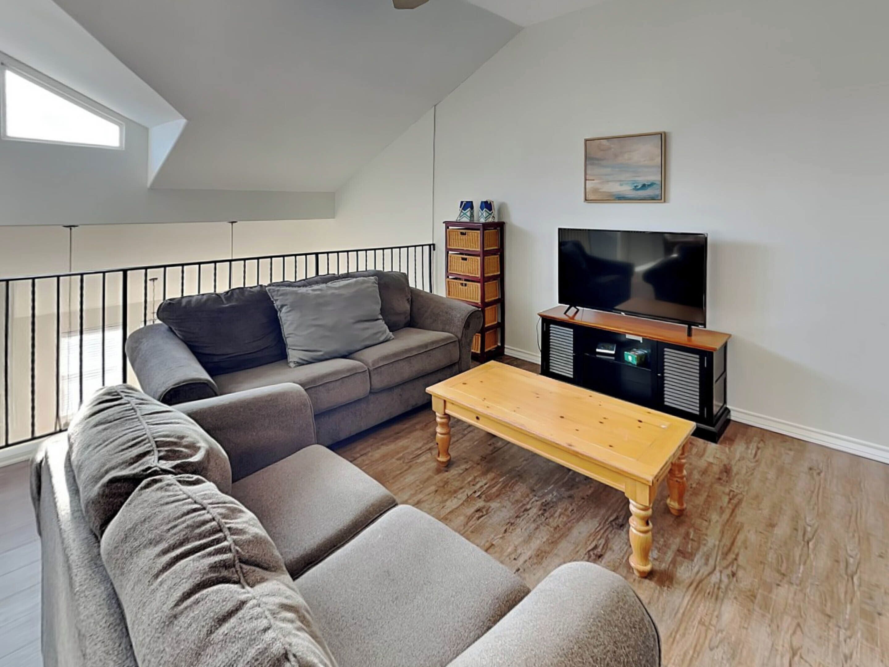 A modern living room with a grey sofa, a wooden coffee table, and a TV on a wooden stand.