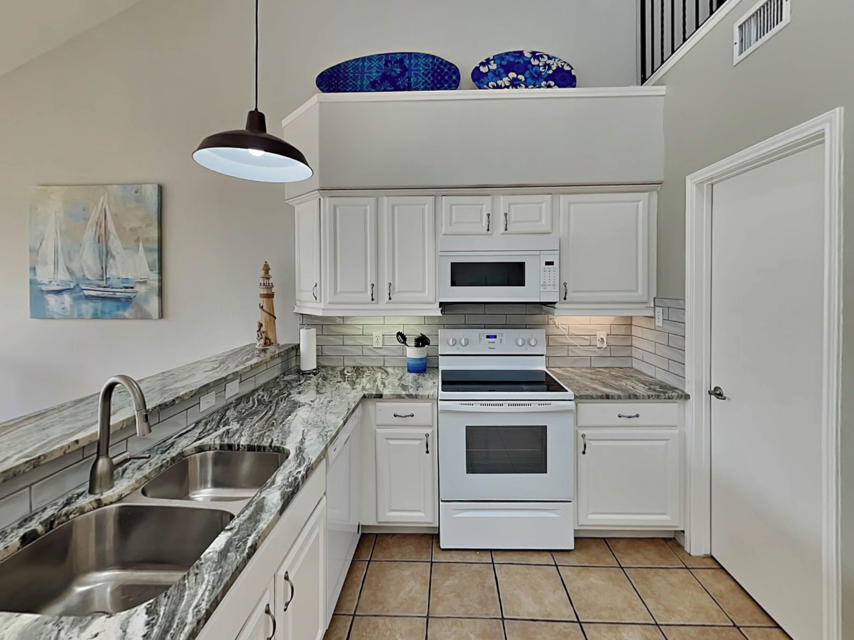 A kitchen with white cabinets, a double oven, a microwave, and a sink.