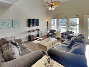 A modern living room with a sofa set, a coffee table, a TV, and a ceiling fan. - Sol Searcher by Silver Sands Vacation Rentals (Port Aransas)