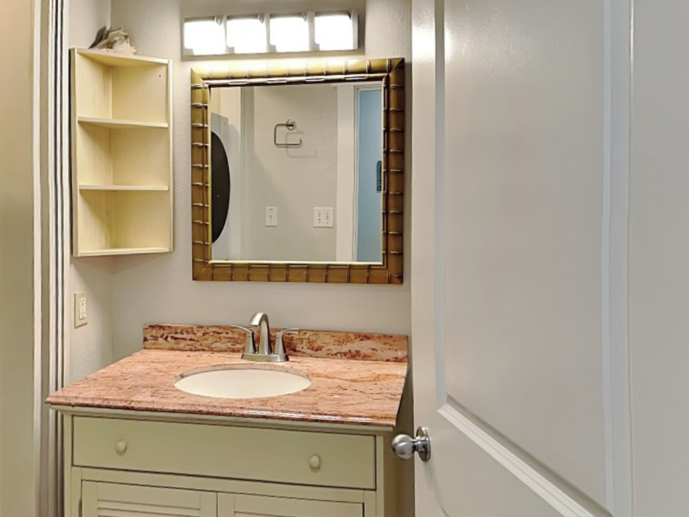 A bathroom with a sink, mirror, and a small shelf.