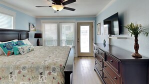 Un dormitorio con cama, cómoda, ventilador de techo y televisor en la pared.