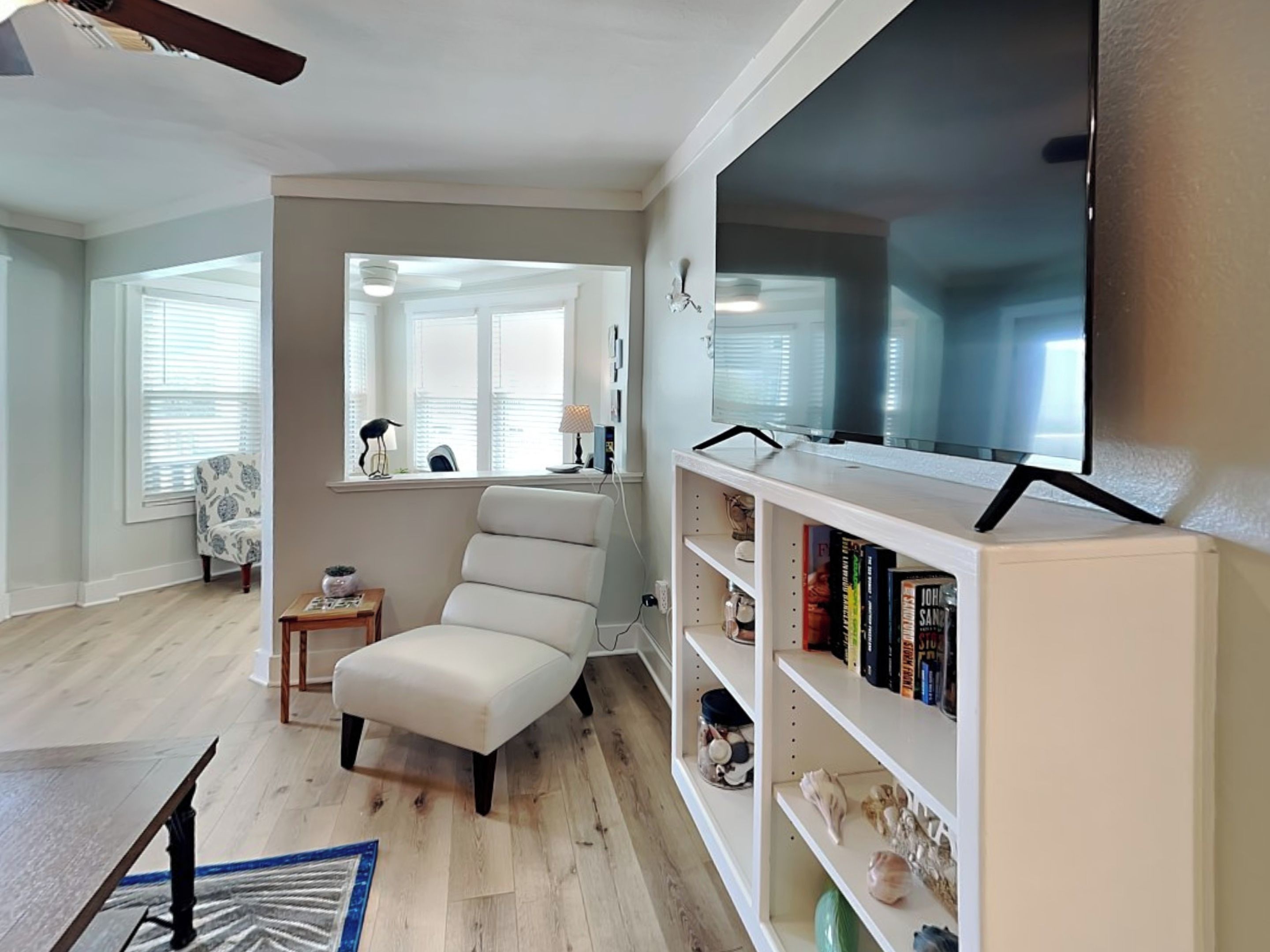 A living room with a white armchair, a bookshelf, and a flat-screen TV mounted on the wall.