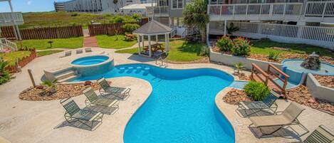 A swimming pool with lounge chairs, a gazebo, and a multi-story building with balconies.