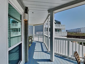 A covered outdoor area with a wooden deck, white railings, and a view of a building with multiple balconies.