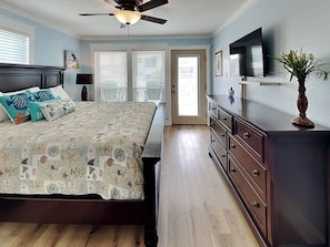 A bedroom with a bed, dresser, ceiling fan, and a TV on the wall.
