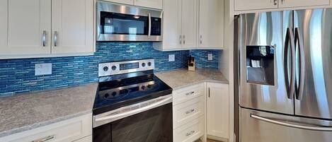 A modern kitchen with white cabinets, a stainless steel refrigerator, a built-in oven, and a microwave.