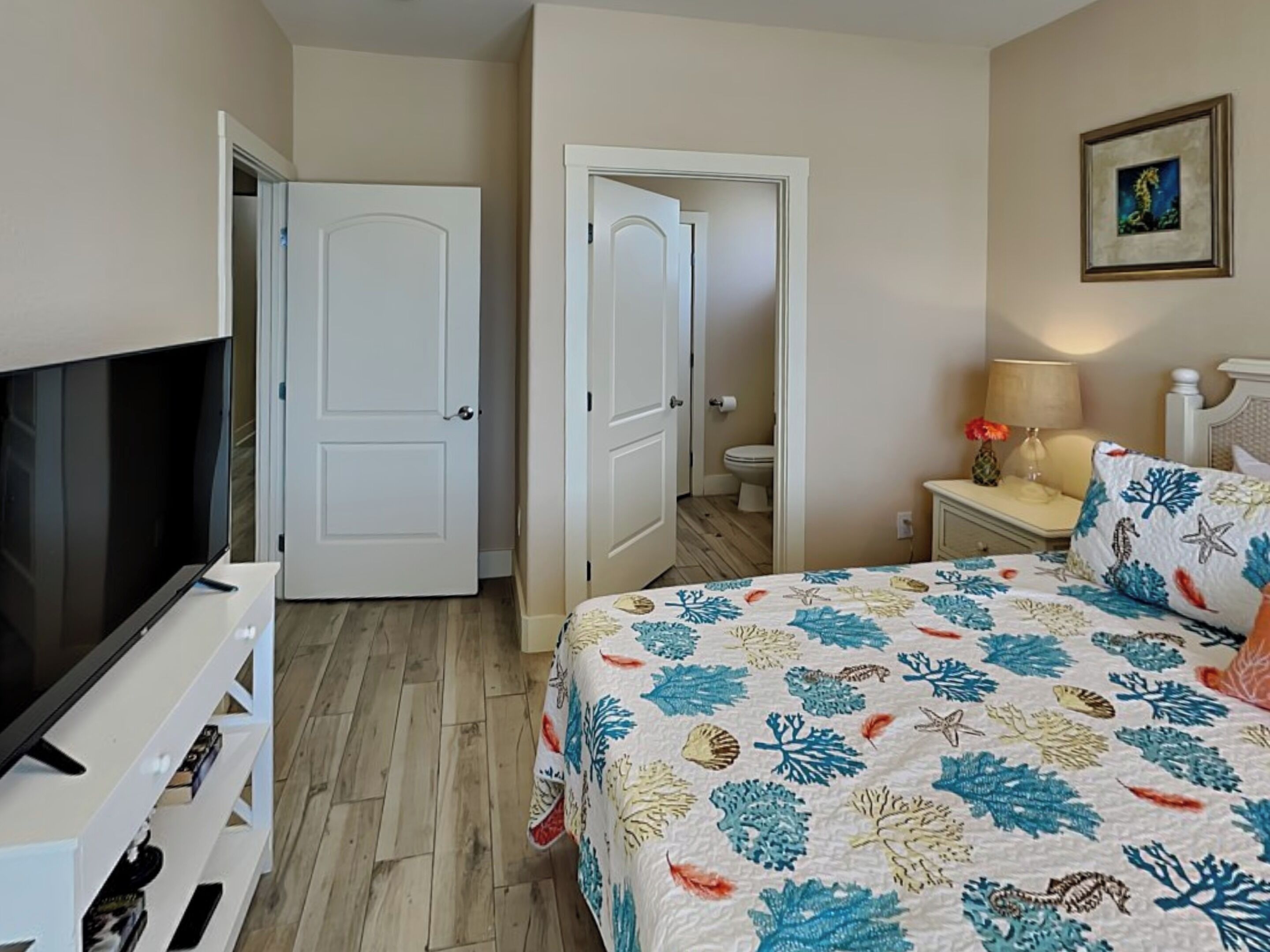 A bedroom with a bed, a TV, a nightstand, a lamp, and a framed picture on the wall.