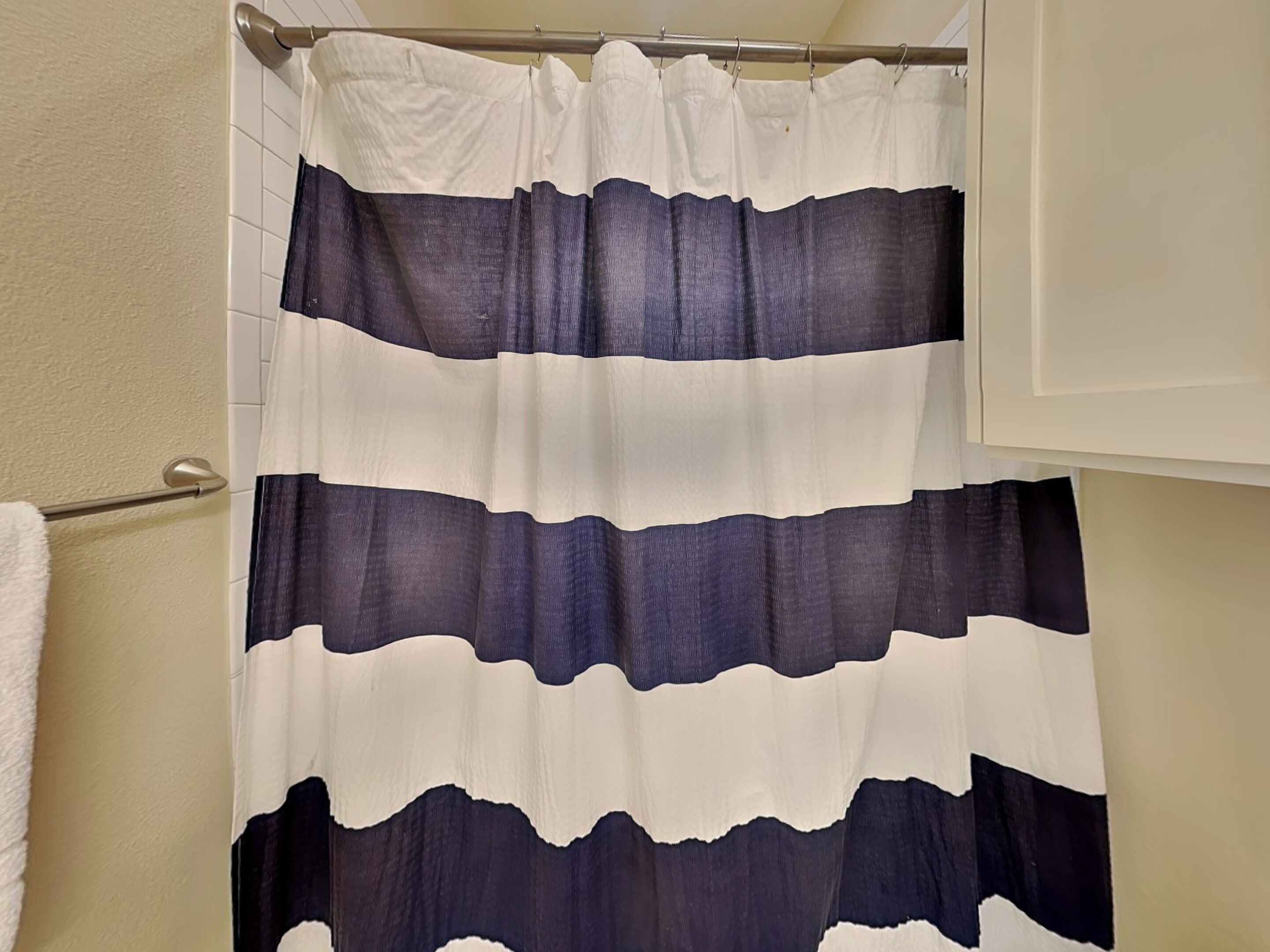 A bathroom with a shower curtain featuring horizontal stripes in white and dark blue.