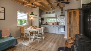 A cozy kitchen with white cabinets, a dining table with chairs, a ceiling fan, and a wood-burning stove. - Cozy Home in Rudzienice (Rudzienice)