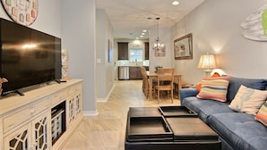 A modern living room with a flat-screen TV, a blue sofa, and a dining area with wooden chairs and a table. - Surfin' Seahorse by Silver Sands Vacation Rentals (Port Aransas)