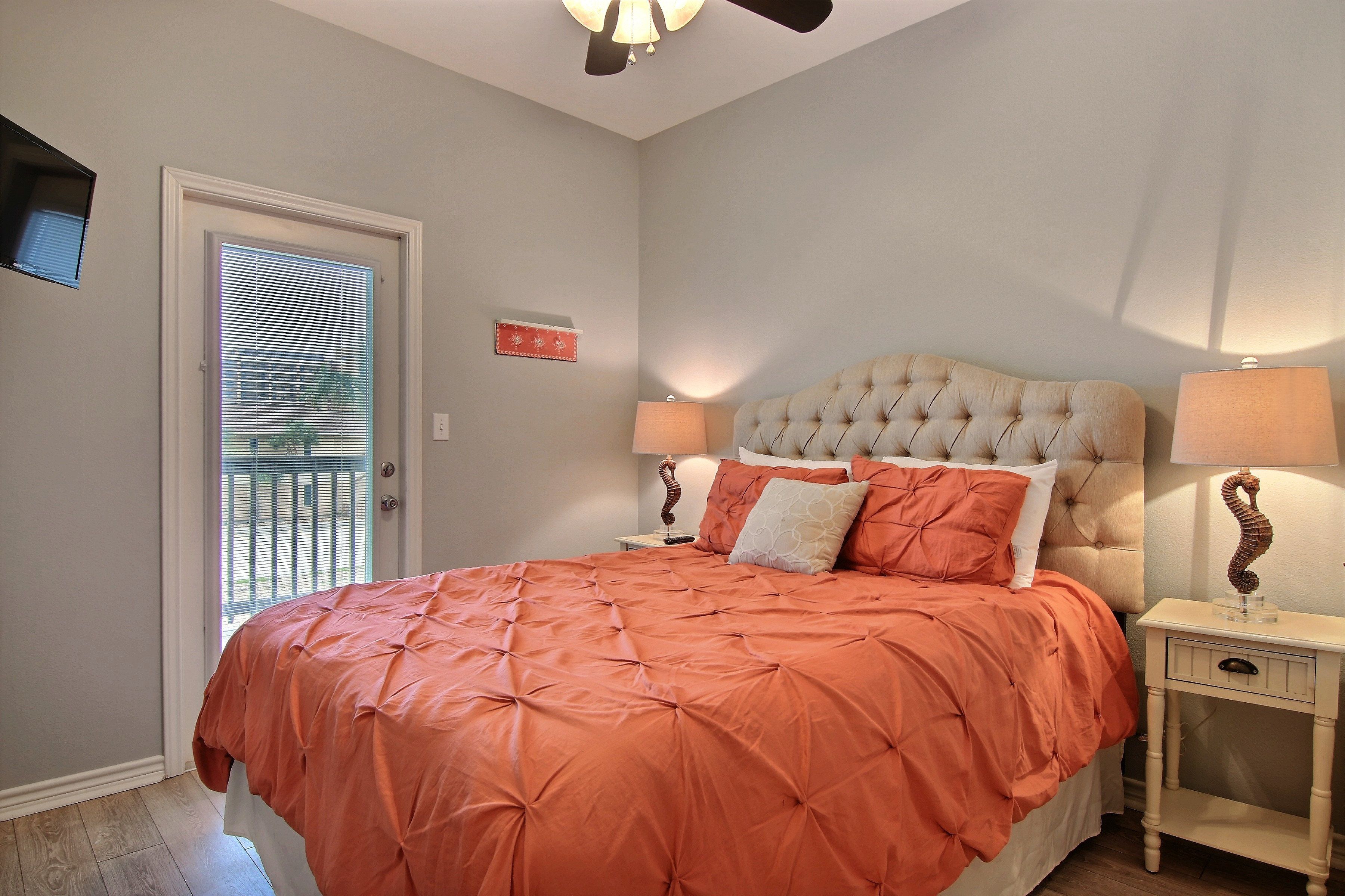 A bedroom with a large bed, two bedside tables, a ceiling fan, and a door with blinds.