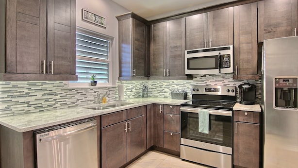 A modern kitchen with dark wood cabinets, stainless steel appliances, and a tiled backsplash. - Surfin' Seahorse by Silver Sands Vacation Rentals (Port Aransas)