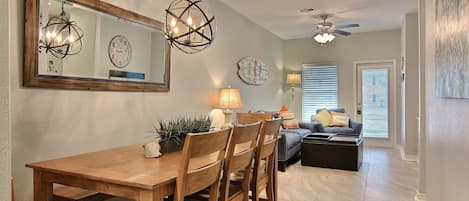A dining area with a wooden table and chairs, a chandelier, and a ceiling fan.