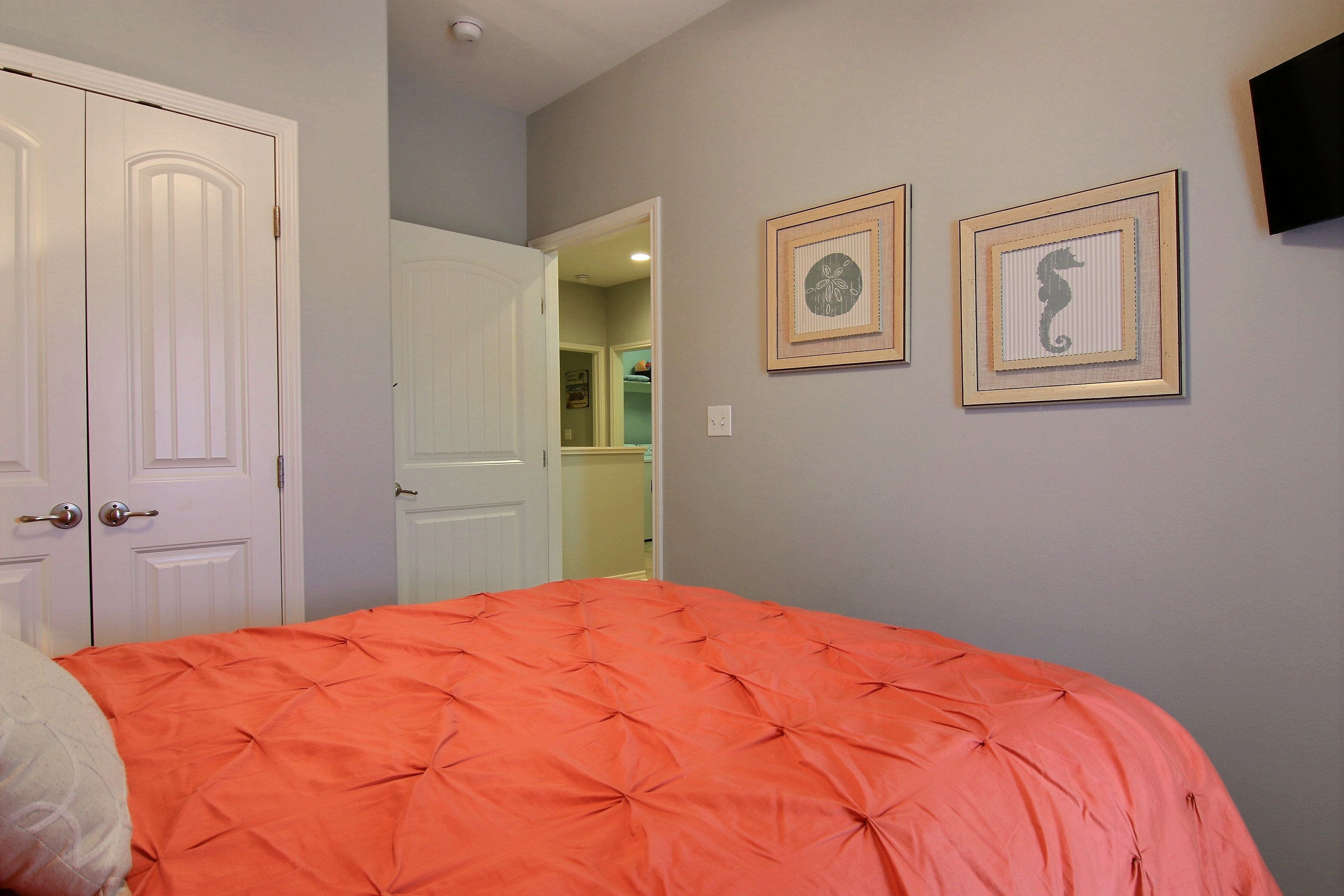 A bedroom with a large bed, white doors, and two framed pictures on the wall.