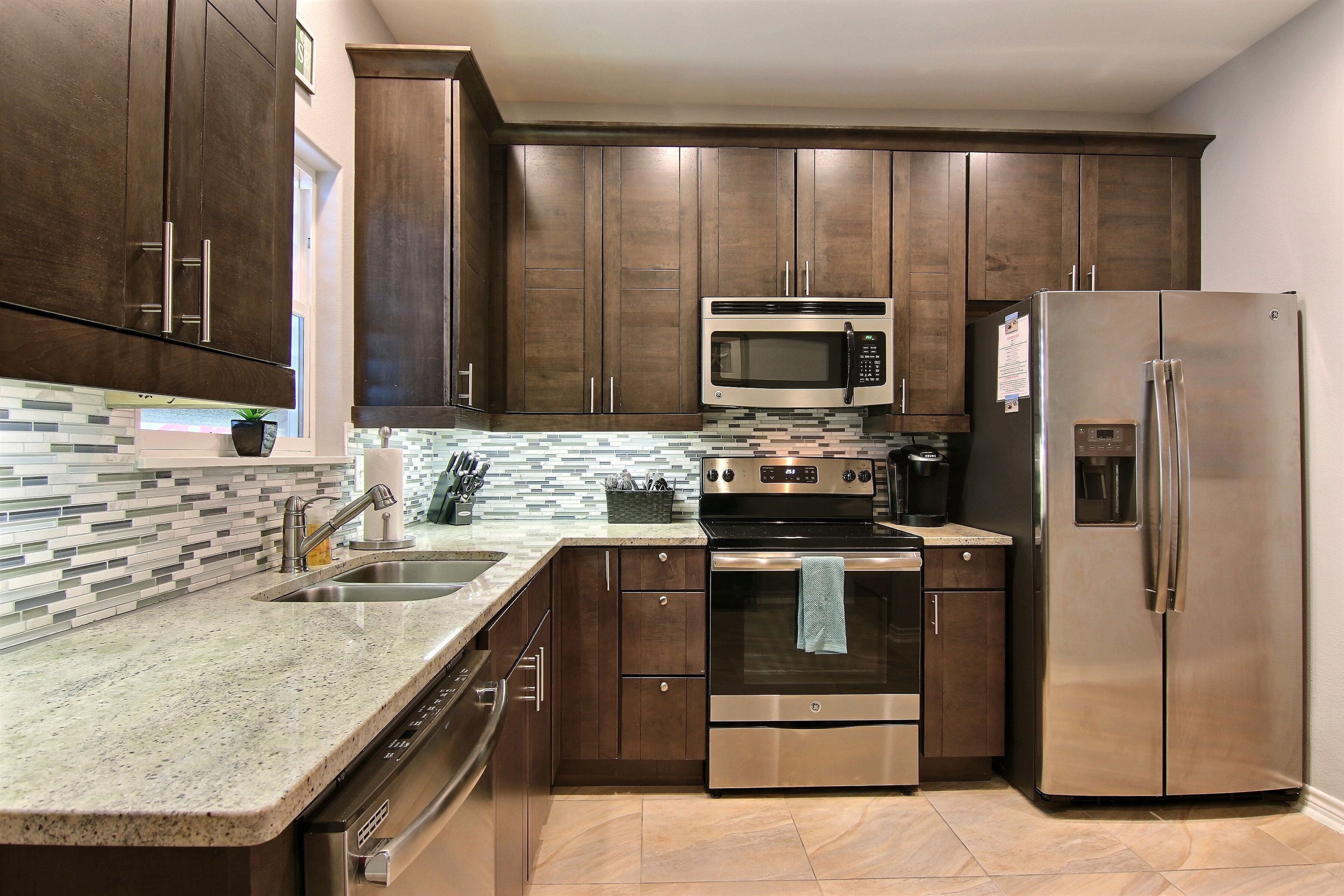 A modern kitchen with dark wooden cabinets, stainless steel appliances, a tiled backsplash, and a granite countertop.