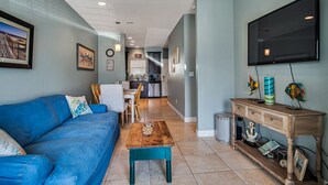 Un salon avec un canapé bleu, une table basse en bois et un téléviseur fixé au mur.