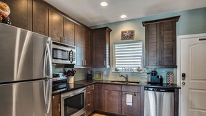 Une cuisine moderne avec des meubles en bois foncé, des appareils électroménagers en acier inoxydable, une fenêtre avec des stores et un panneau indiquant qu'il est interdit de fumer.