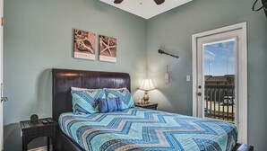 Une chambre à coucher avec un lit, une table de chevet, un ventilateur de plafond et des œuvres d’art accrochées au mur.