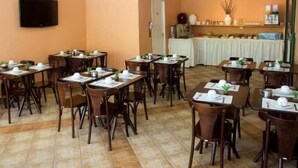 A dining area with multiple tables and chairs, a television mounted on the wall, and a kitchen area with a counter and various items on display. - Vicz Palace Hotel (Curitiba)