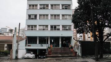 Um edifício com vários andares, fachada plana, grandes janelas e escadaria que dá acesso à entrada.