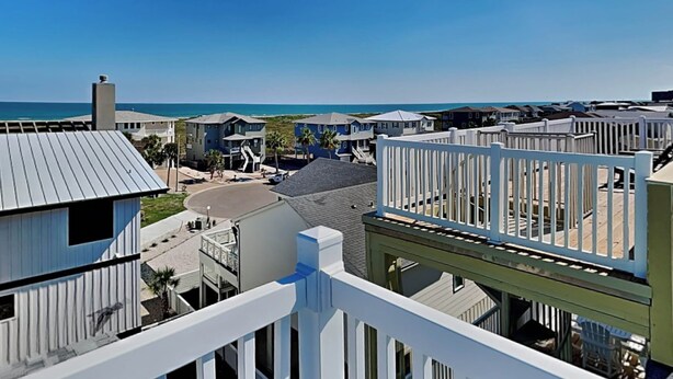 A coastal residential area with houses, a white fence, and a view of the ocean. - The Fire Escape by Silver Sands Vacation Rentals (Port Aransas)