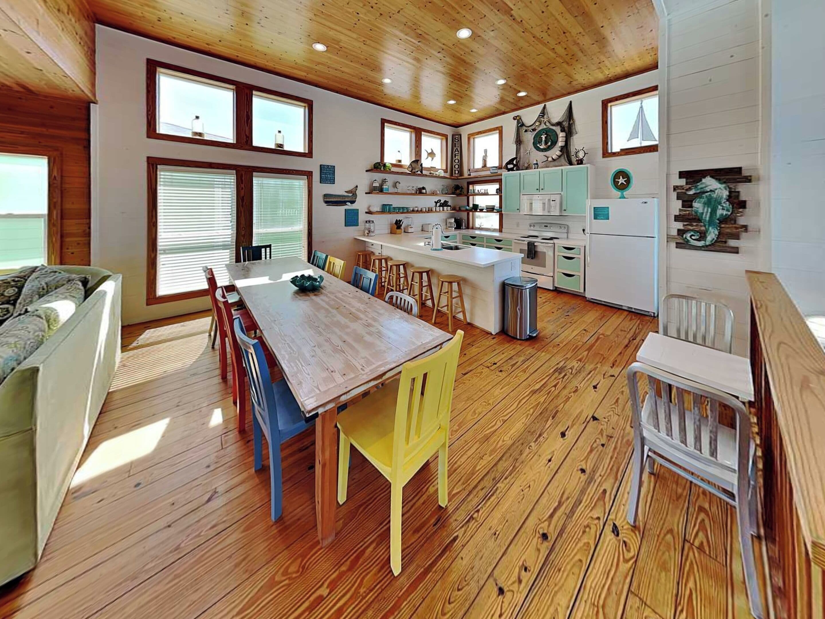 A spacious kitchen with wooden flooring, a central island, and a dining area with colorful chairs.