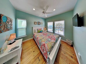 A bedroom with a bed, a desk, a ceiling fan, and two windows.