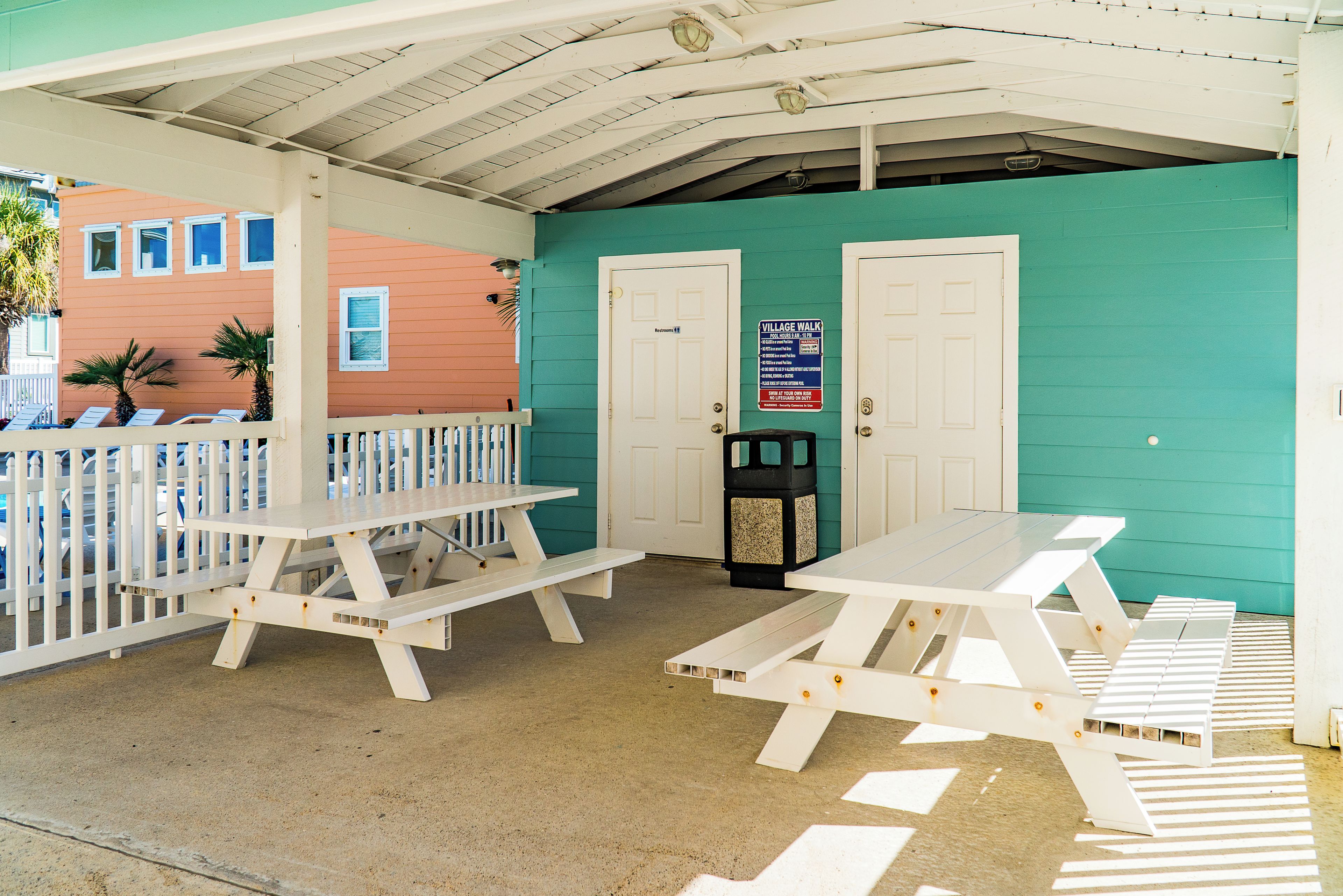 A covered outdoor area with picnic tables and a trash can.