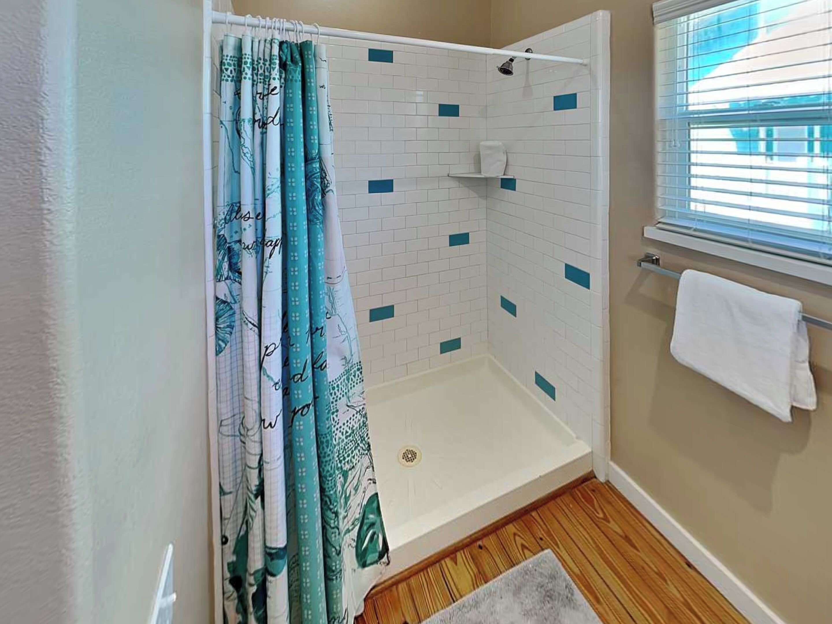 A shower area with a white tiled wall, a white shower curtain with a pattern, and a white towel hanging on a rack.