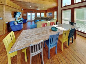 A wooden interior with a dining table, chairs, a sofa, and a television.