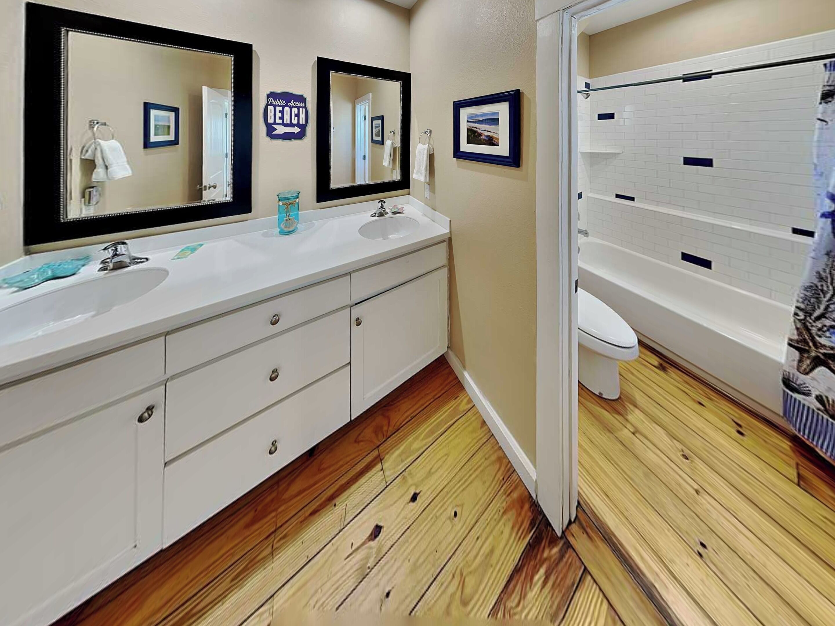 A bathroom with a wooden floor, two sinks, a toilet, and a bathtub.