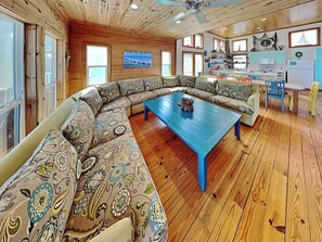 A cozy living room with a large sectional sofa, a blue coffee table, and a wooden ceiling with a ceiling fan. - The Fire Escape by Silver Sands Vacation Rentals (Port Aransas)