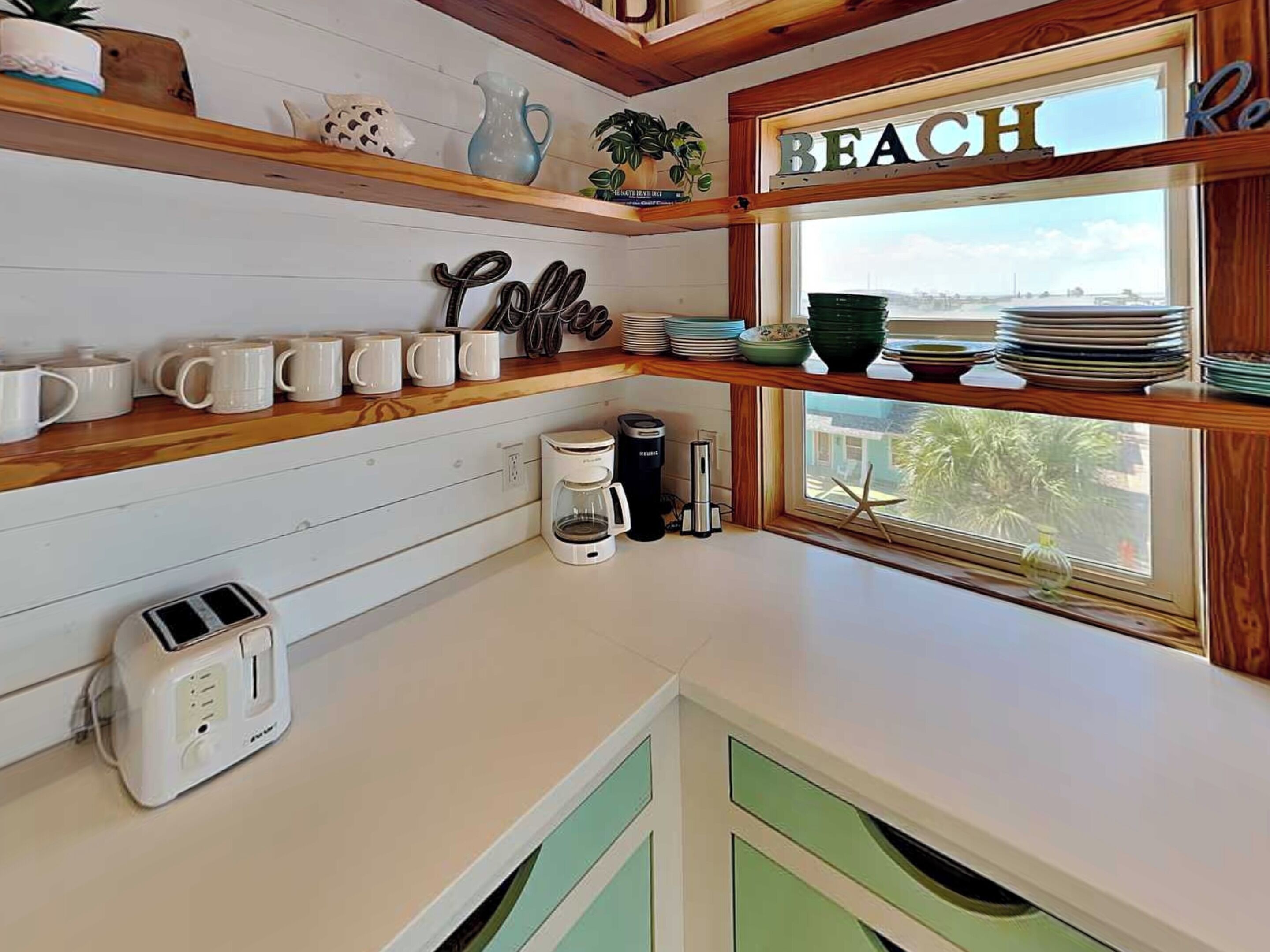 A kitchen with wooden shelves, a coffee maker, a toaster, and a window with a view.