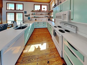 A kitchen with white cabinets, wooden flooring, and a microwave.
