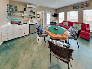 A room with a dining table, chairs, a red sofa, a television, and a wall-mounted air conditioner.