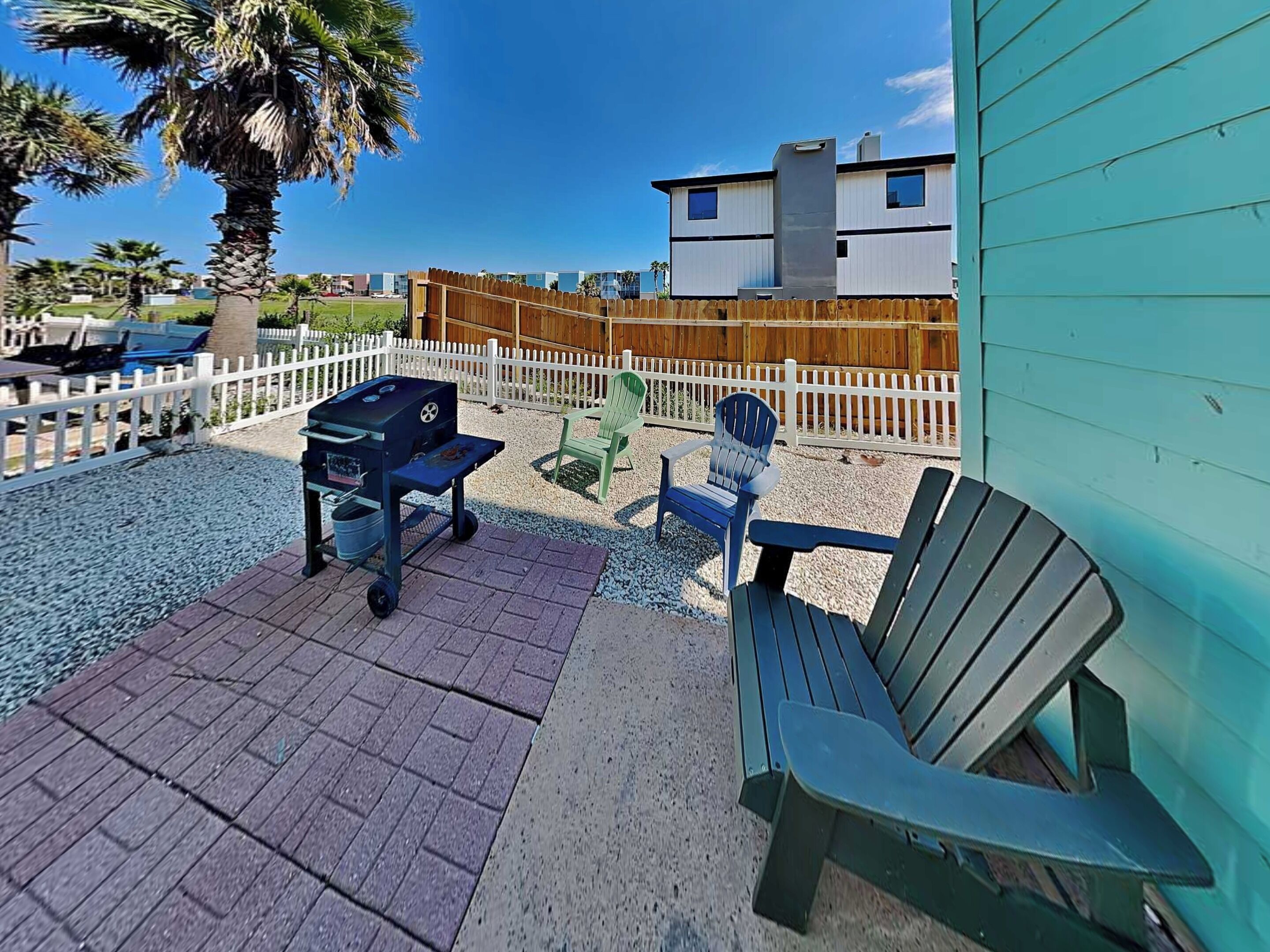 Une terrasse avec un barbecue, deux chaises Adirondack et une clôture en bois.