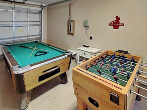 Une table de billard et une table de baby-foot dans une pièce dont le fond est constitué d’une porte de garage.