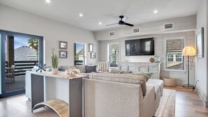 Ein modernes Wohnzimmer mit einer Couch, einem Couchtisch und einem Fernseher. Eine Deckenventilator und ein Fenster mit Jalousien sind vorhanden.