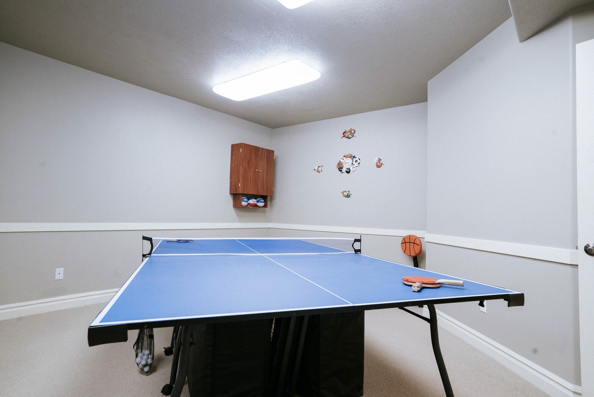 Ein Raum mit einem Tischtennisschläger, einem Schrank voller Sportbälle und Wanddekorationen zum Thema Sport.