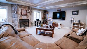 A living room with a stone fireplace, a large flat-screen TV, and a comfortable brown leather sofa. - Family FUN at the Homestead with Pool & Ping Pong, Karaoke & more! Great Value! (Brigham City)