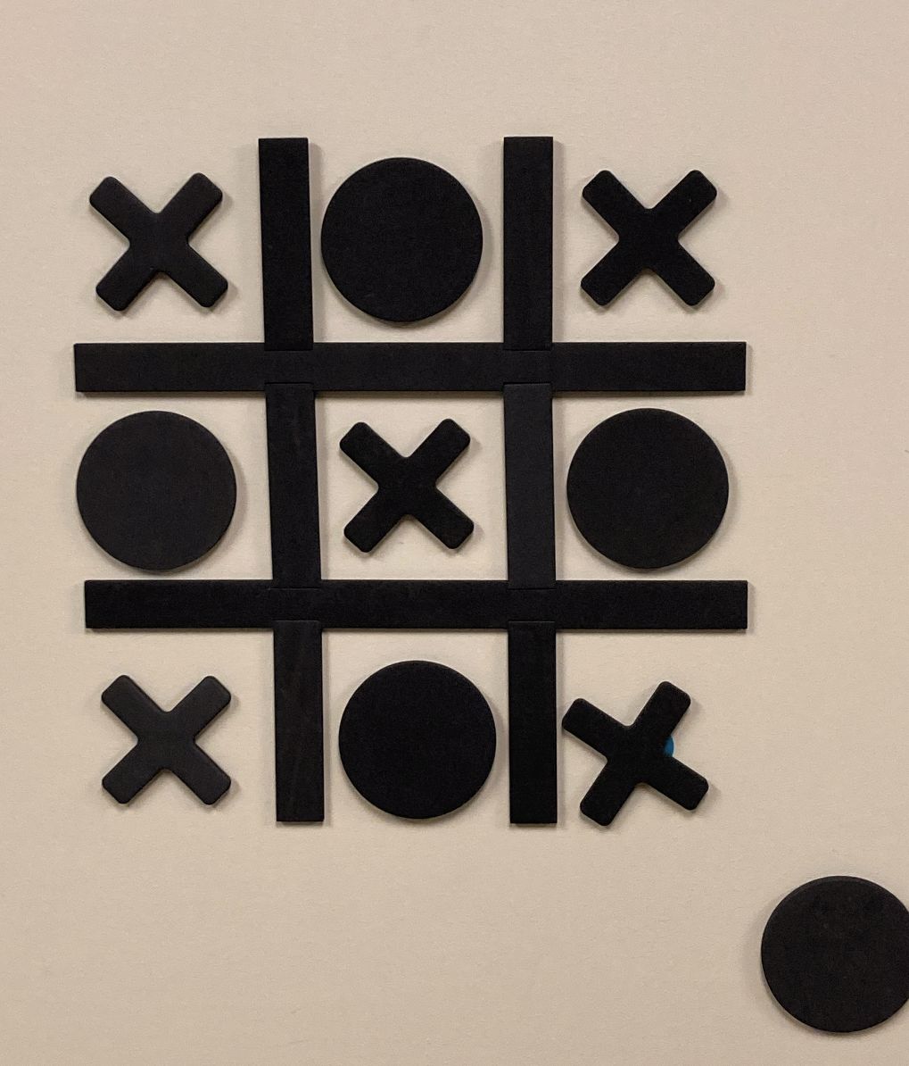 En spelplan för tic-tac-toe med svarta X och O-brickor på en beige vägg.