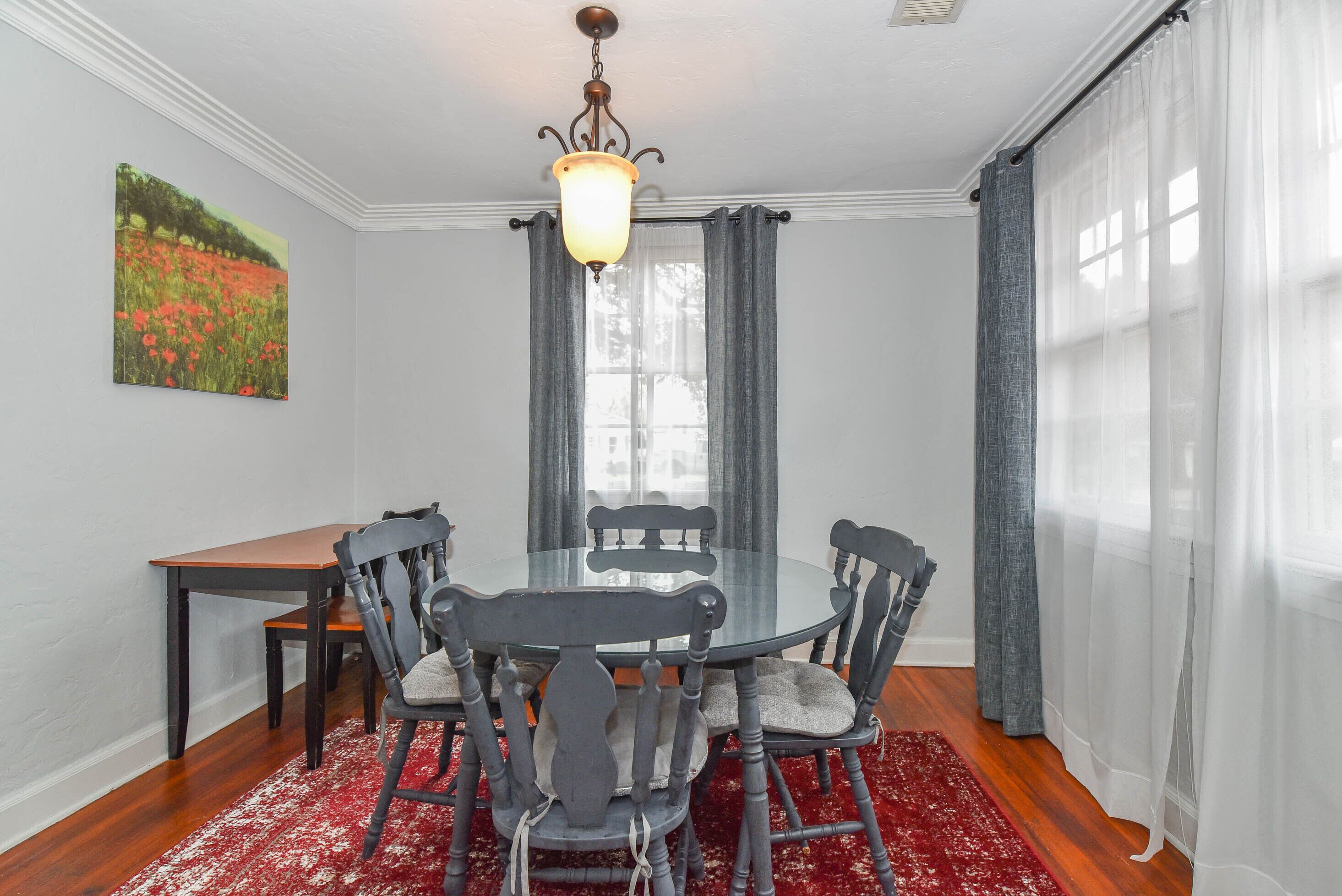 A dining area with a round table, six chairs, a small side table, and a red patterned rug.