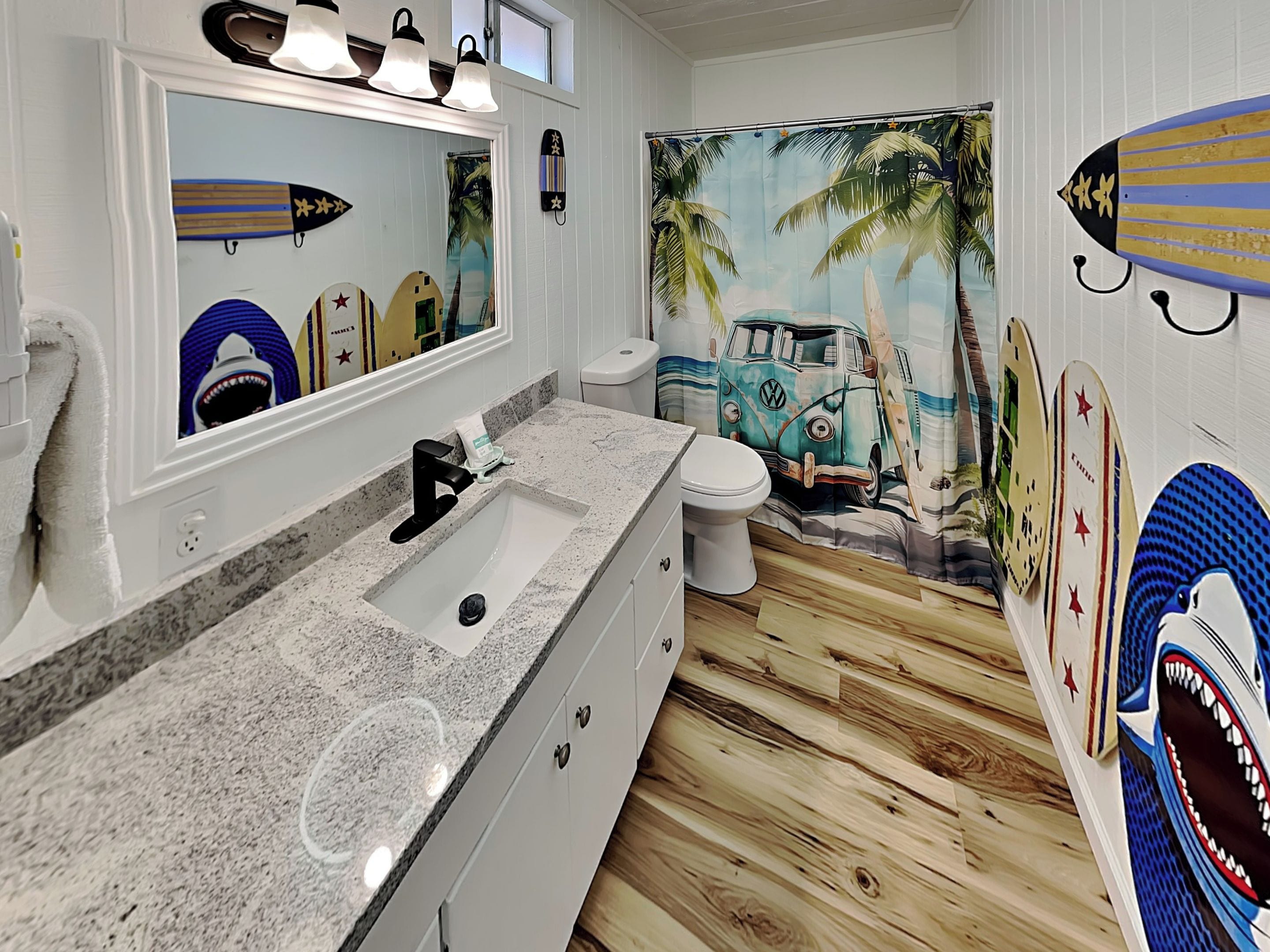 A bathroom with a vanity, sink, mirror, and a wall mural featuring surfboards and a van.