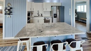 Cozinha moderna com uma ilha grande, banquetas brancas e um espaço para vinhos na parede.
